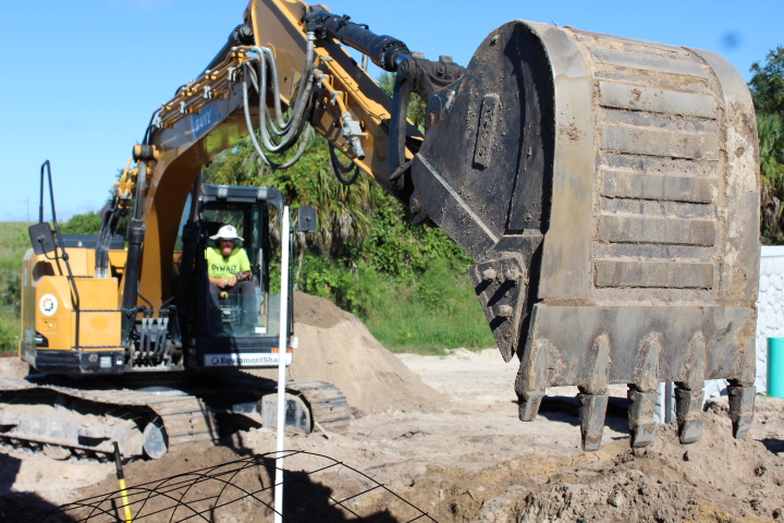 A crewperson mans the excavator behind the main building.