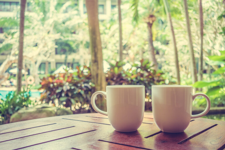 Two coffee mugs on a wooden table beside a window in soft morning light.
